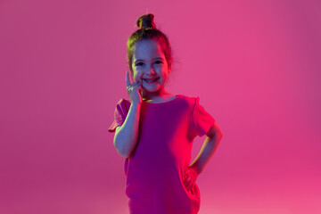 Charming cute little girl, kid wearing pink t-shirt posing isolated on magenta color background. Concept of children emotions, fashion, beauty, school and ad concept