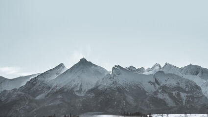 Distant winter mountain ridge panorama with rocky peaks. Dramatic view of mountains with snow-covered summit. Polish tatry in winter.