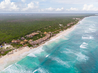 Aerial drone view of Tulum beach between tropical green jungle and wavy Caribbean Sea with human constructions on a cloudy day