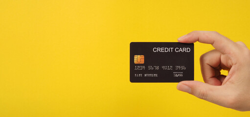 Hand is holding black credit card on yellow background.