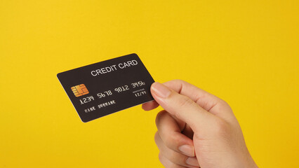 Hand is holding black credit card on yellow background..