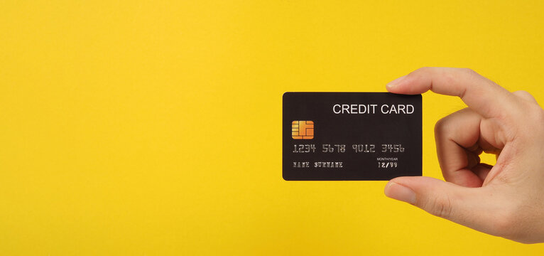 Hand Is Holding Black Credit Card On Yellow Background.