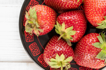 Several berries of juicy sweet strawberries with a ceramic plate on a wooden table, close-up, top view.