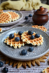 vertical composition. Waffles with blueberries on plates on a wooden table. Closeup