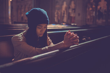 Young woman prayer's pray alone in church, People pray to God with folded hands, old wooden classic long chairs background - obrazy, fototapety, plakaty