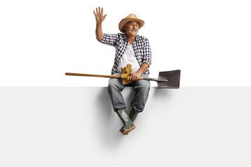 Full length portrait of a mature farmer with a spade sitting on a blank panel and waving