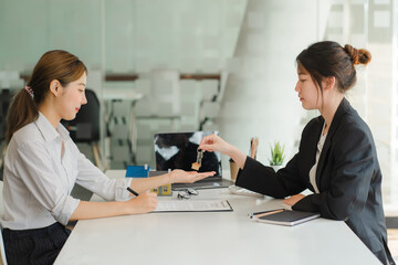 A saleswoman checks the lease and holds a small gray model of house and house keys in preparation for meeting customers to sign the lease. Real estate leasing concept.