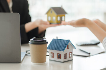 A saleswoman checks the lease and holds a small gray model of house and house keys in preparation for meeting customers to sign the lease. Real estate leasing concept.
