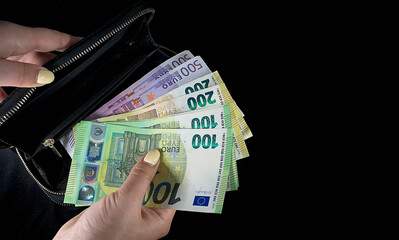 Euro bills in the hands of a man in a black wallet on a black background