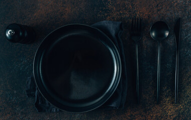 Black table setting with plate, linen napkin and cutlery over black background. Minimal concept.