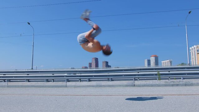 Guy with naked torso doing backflip four times on embankment. Male gymnast, acrobat practising salto backward on city river esplanade. Sportsman training outdoor. Young man does sport outdoor