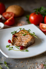 A hearty lunch, a romantic dinner. Grilled French steak with thyme and cranberries on a beautiful white plate on a gray background. Vertical photo. Close-up.