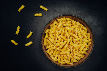 Raw spirelli or fusilli in a bowl photographed from above on a dark table