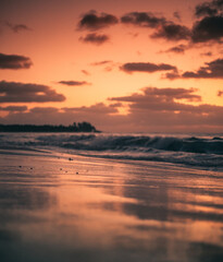 Orange sunset at the beach with waves crashing and light reflection on a cloudy morning in Tulum 