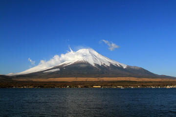 Fuji mountain with snow and fog covered top, lake or sea and clear blue sky background with copy space. This place famous in Japan and Asia for people travel to visit and take picture.