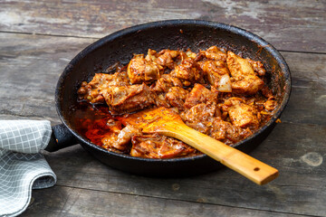 Fried chicken in a frying pan with a wooden spatula on a dark table.