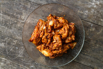 Fried chicken in sauce in a glass plate on a dark wooden table.