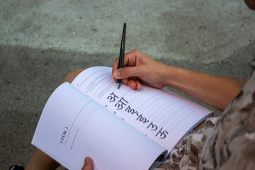 a student is sitting outside and writing in a Sanskrit workbook