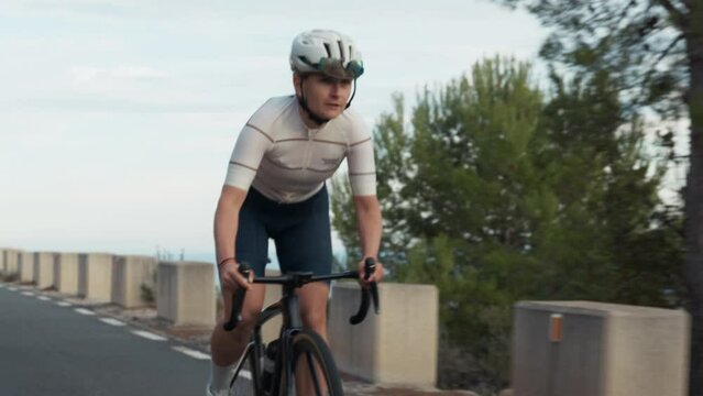 Close up of professional confident road cyclist, young pretty energetic strong woman rides bike on high mountain road on daily activity difficult sport hard training. Healthy outdoor lifestyle