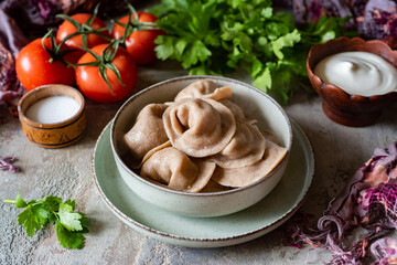 Healthy lunch for the whole family: Boiled rye dumplings with meat filling in a beautiful plate on a gray background. Dumplings made of rye flour dough with pork meat filling. Close-up