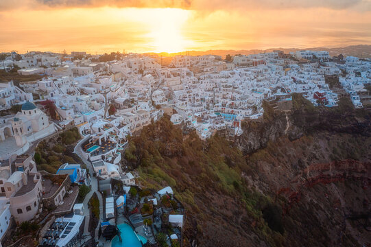 Santorini, Imerovigli village on the cliff with caldera view at sunrise, scenic aerial landscape with white architecture, Aegean Sea, colored sky with clouds and sun, outdoor travel background, Greece