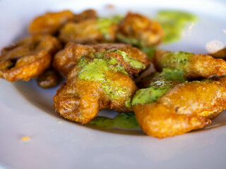 Fried mushrooms lie on a white plate with green sauce