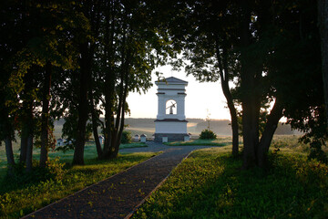 Obraz premium Early summer morning. Sunrise. Belarus. Novogrudsky region. White outlines of a historical kaplitsa are visible through black contours of trees of the avenue.