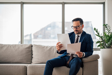 Confident businessman reading documents while sitting on sofa at office
