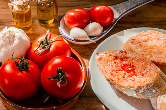 Receta t&iacute;pica Catalu&ntilde;a. Pan con tomate untado y aceite sobre encimera de madera y un bol con ajos. 