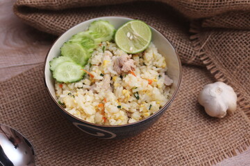 Pork Fried Rice, Chinese Style Fried Rice in a Bowl with Cucumber and Lemon Served on a brown wooden table.