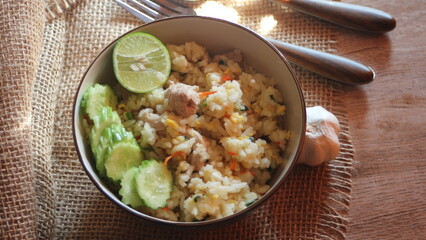 Pork Fried Rice, Chinese Style Fried Rice in a Bowl with Cucumber and Lemon Served on a brown wooden table.