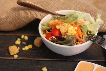 Caesar salad in white bowl served with Caesar dressing. on a black wooden table.