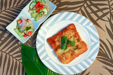 Fried bread with minced pork spread with cucumber dipping sauce on a wooden table.