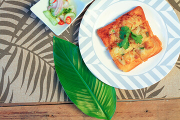 Fried bread with minced pork spread with cucumber dipping sauce on a wooden table.