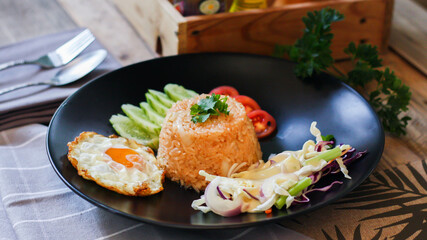 Fried rice, fried egg, cucumber, sliced tomato, green salad and Fried chicken placed on a black plate as a garnish.
