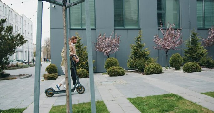 Two smiling colleagues going downtown street talking. Office managers commuting to work with eco-friendly vehicles. Technology, partnership, occupation concept.