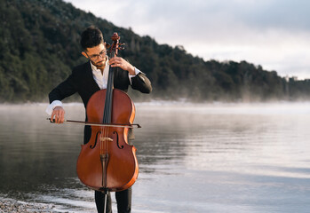 Musician playing cello by the lake on a misty morning