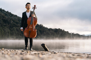 Musician about to play his cello by the lake on a misty morning