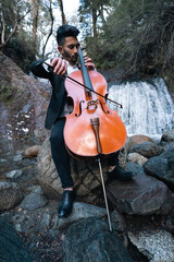 musician playing cello by a waterfall wearing glasses