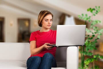 Young woman student using laptop in a video call or online class while sitting on sofa at home