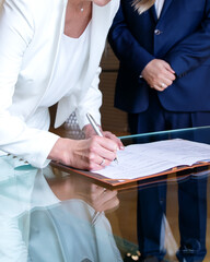50-years old bride and groom signing marriage agreement at desk. Woman's hand holding pen and...