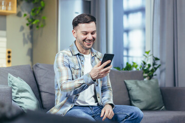 Portrait of a young handsome man. Sits at home on the couch, talking on the phone, writes a story Waving his hands, explains