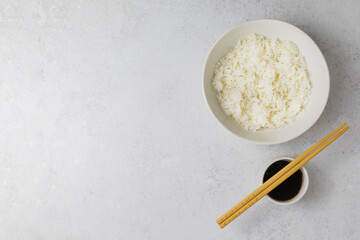 A bowl of rice, soy sauce and chopsticks on white background. Top view, copyspace