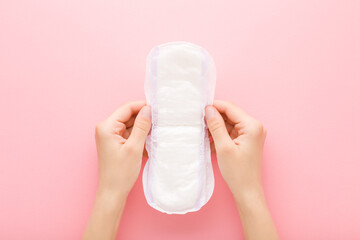 Young adult woman hands holding opened white big size sanitary towel on pink table background....
