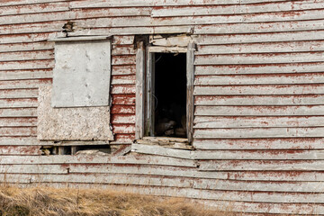 The exterior wall of a textured grungy wooden worn red building. The wall has a small open window...
