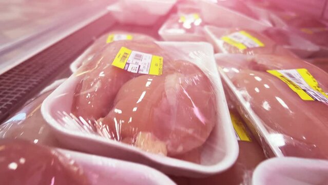 Raw chicken and turkey fillet in plastic containers wrapped in cling film are on the showcase of the refrigerator in the supermarket. Closeup