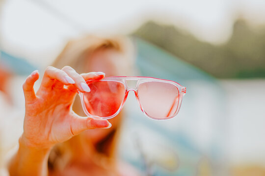 Woman in deep pink bikini showing pink sun glasses to the camera. Beach concept. Focus is on glasses.