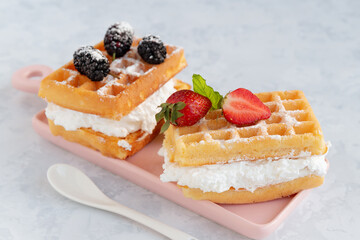 Close up of two delicious waffle sandwiches on a rectangular plate with spoon on light grey background. Selective focus, blurred background.