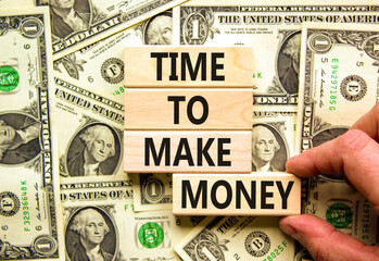 Time to make money symbol. Concept words Time to make money on wooden blocks on a beautiful background from dollar bills. Businessman hand. Business, finacial and time to make money concept.