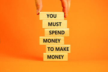 Spend and make money symbol. Wood blocks with words You must spend money to make money. Beautiful orange table orange background Businessman hand. Business spend and make money concept. Copy space.